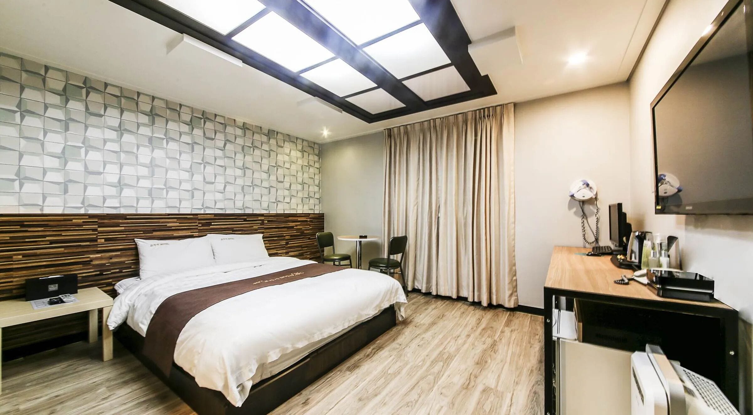 Habitación de hotel con cama, escritorio, silla, espejo y ventana con cortinas.