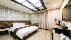Habitación de hotel con cama, escritorio, silla, espejo y ventana con cortinas.