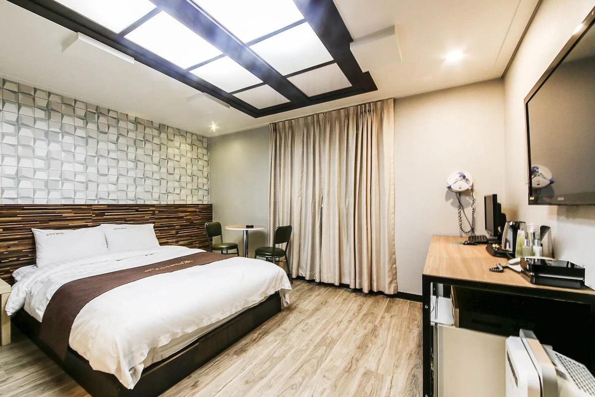 A hotel room with a bed, a desk, a chair, a mirror, and a window with curtains.