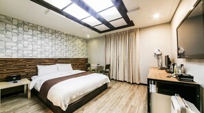 A hotel room with a bed, a desk, a chair, a mirror, and a window with curtains. - KOZAZA (Changwon-si)