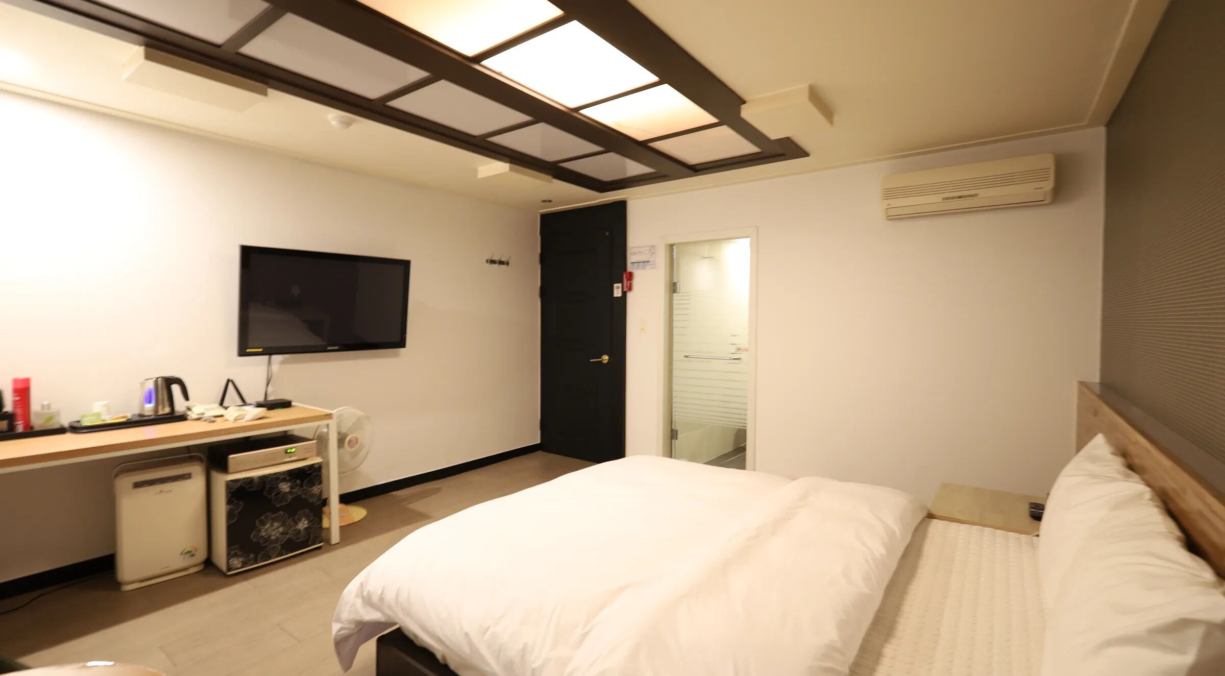 A hotel room with a bed, a desk with a computer, a television, and a door leading to a bathroom.