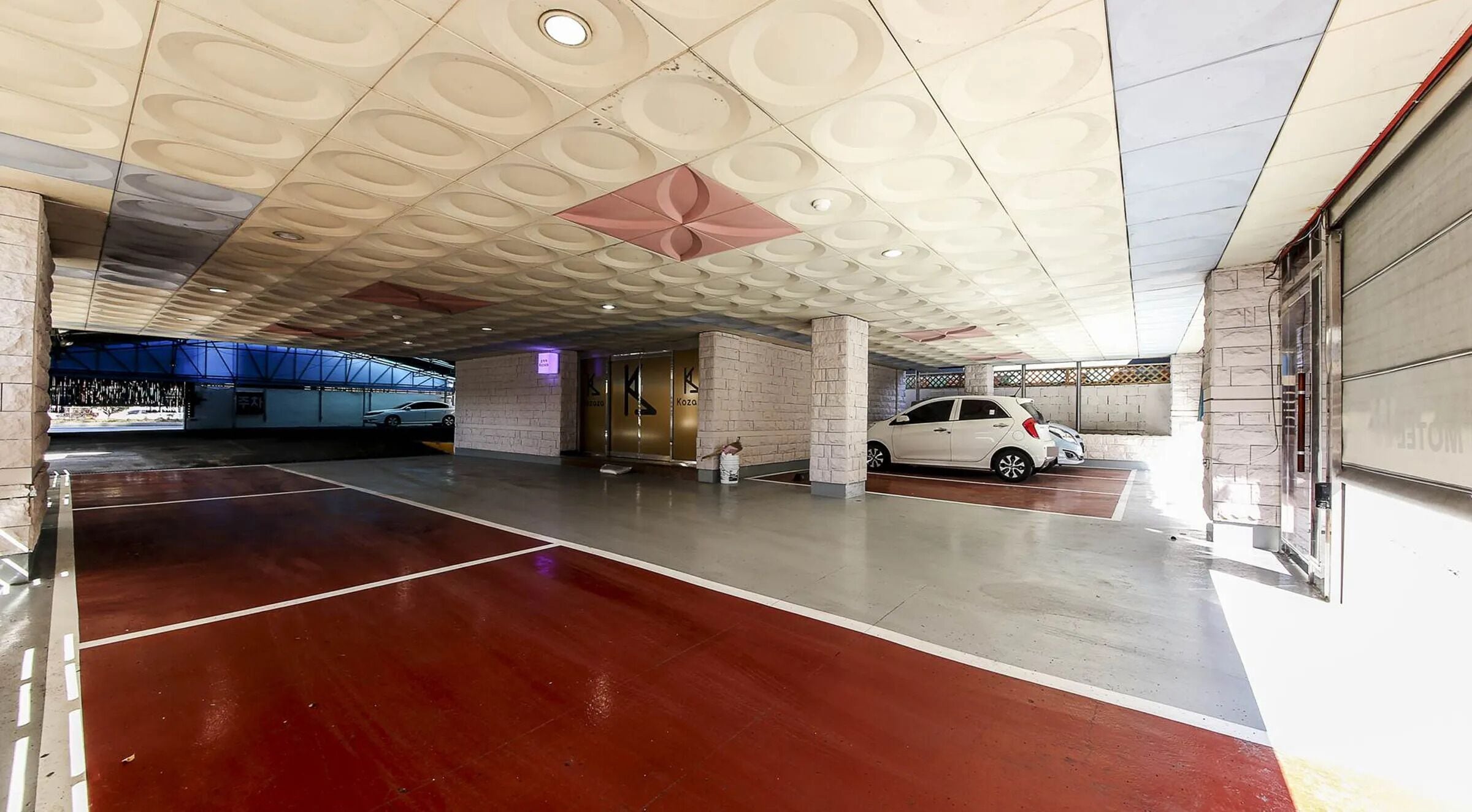 Un área de estacionamiento interior con piso rojo, un automóvil blanco estacionado y un techo con diseños circulares.