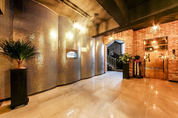 A hotel lobby with a polished marble floor, a textured wall, and a brick wall with a door. - KOZAZA (Changwon)