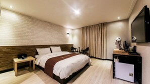 Habitación de hotel con cama, mesita de noche, escritorio, silla, televisor y un minibar.