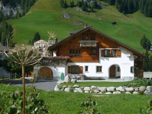 Una casa a due piani in legno, con facciata bianca, un balcone e un cancello in pietra.