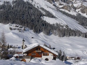 A snow-covered mountain landscape with a wooden cabin and a church with a tower. - Ferienwohnungen Teuriblick A&B, (Splügen), by Interhome (Splügen)