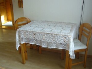 A table with a white lace tablecloth, two wooden chairs, and a wooden floor. - Ferienwohnungen Teuriblick A&B, (Splügen), by Interhome (Splügen)