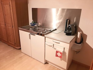 A compact kitchenette with a stainless steel stove, a coffee machine, and a small sink. - Ferienwohnungen Teuriblick A&B, (Splügen), by Interhome (Splügen)