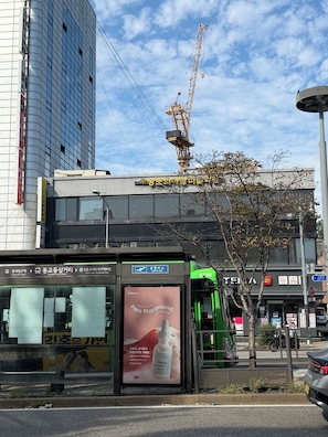 A bus stop with a sign for the airport bus and a billboard advertising a skincare product.
