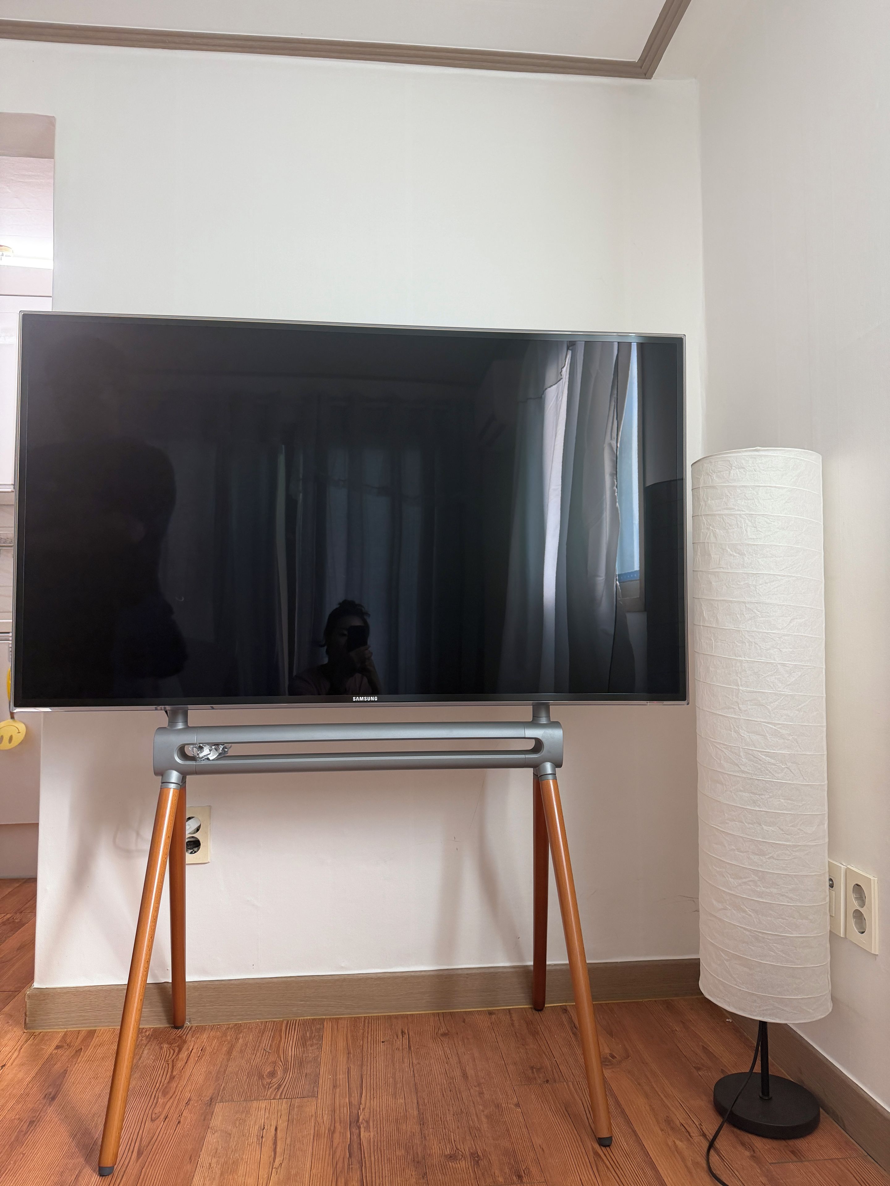 A flat-screen TV on a stand with wooden legs, a lamp, and a wall socket.