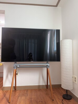A flat-screen TV on a stand with wooden legs, a lamp, and a wall socket.