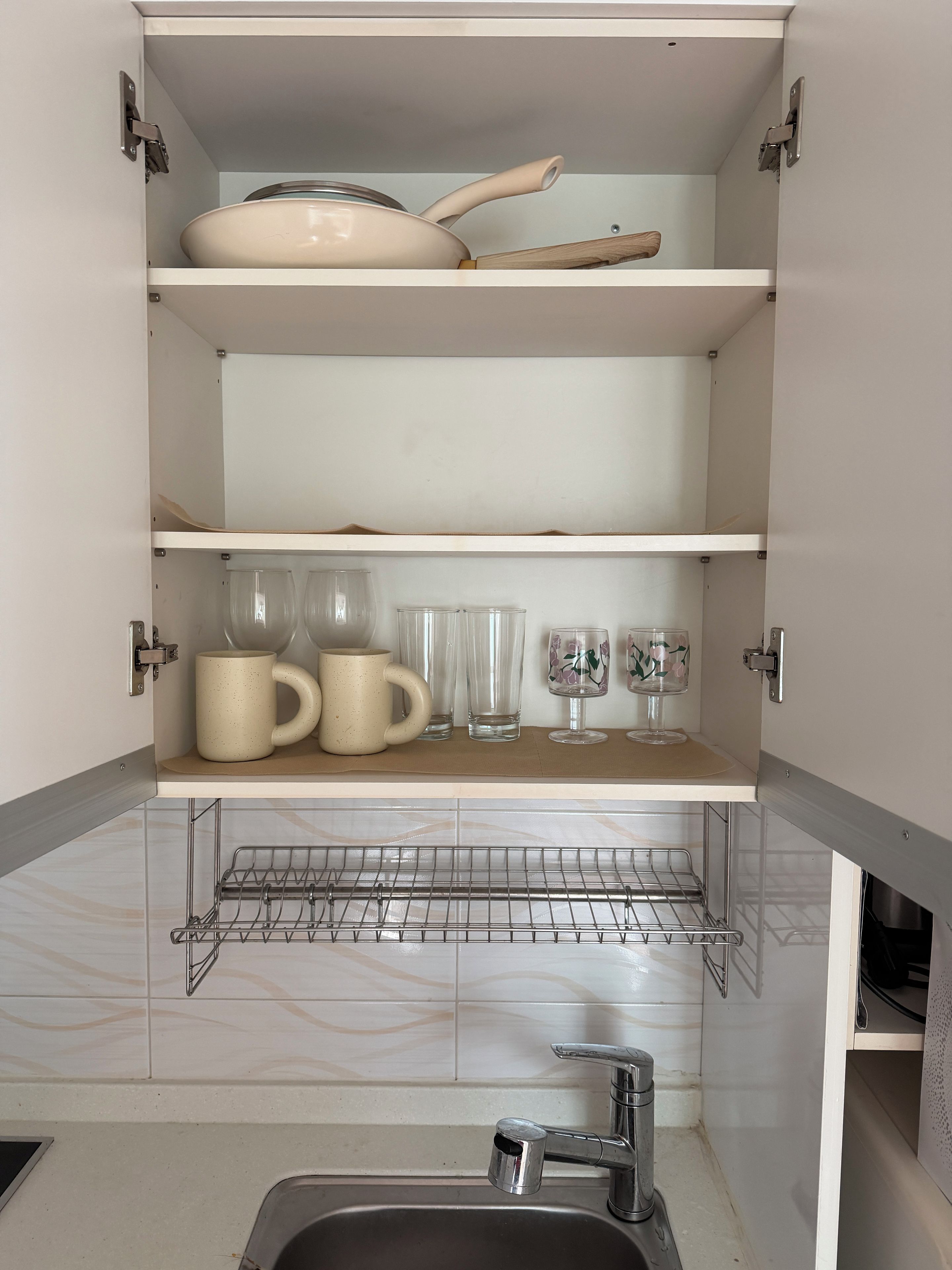 A kitchen with open cabinets, a sink, and a metal rack.