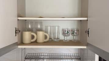 A kitchen with open cabinets, a sink, and a metal rack.