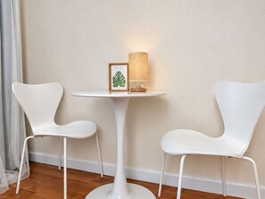 A small white table with a lamp and a framed picture, flanked by two white chairs, against a plain wall.