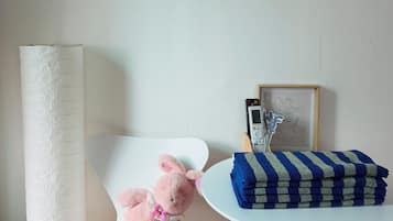 A room with a white chair, a small table with a blue and white striped cloth, a pink stuffed toy, a white lamp, and a framed picture on the wall.