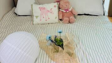 A bed with a striped bedspread, a pillow with a cow design, a teddy bear, and a small bouquet of flowers.