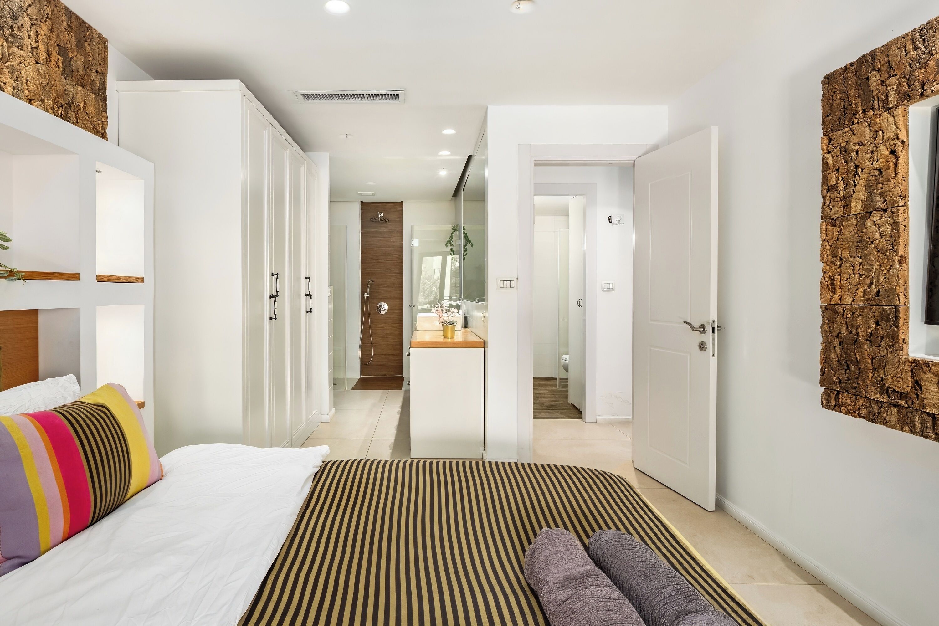 Ein modernes Schlafzimmer mit einem Bett, Nachttischen und einem durchgehenden Türspalte sichtbaren Badezimmer.