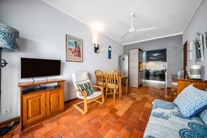 A living room with a television, wooden furniture, a ceiling fan, and a kitchen area. - Pé na Areia House, Armação de Pêra (Armação de Pêra)