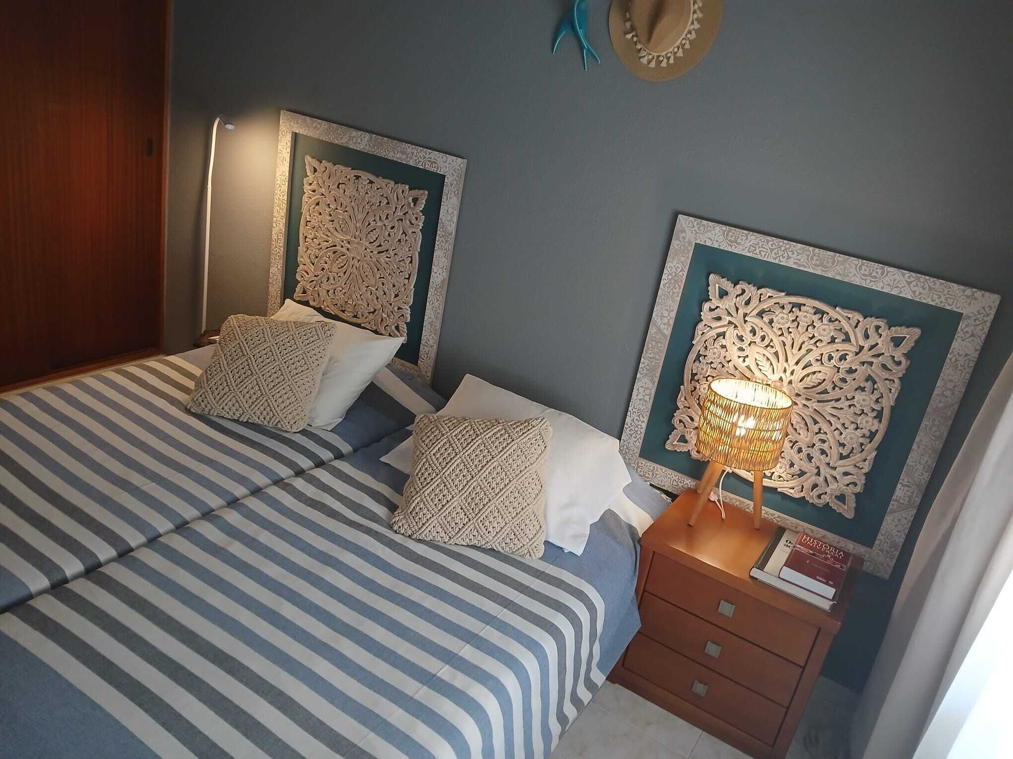A bed with striped bedding, two pillows, a bedside table with a lamp, and decorative wall art.