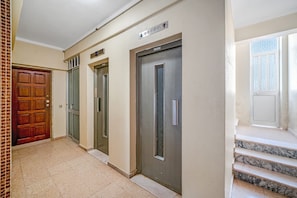 A hallway with three elevator doors, a wooden door, and marble steps leading to an upper floor. - Pé na Areia House, Armação de Pêra (Armação de Pêra)