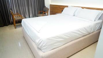 A hotel room with a large bed, a wooden headboard, a chair, and a curtain.
