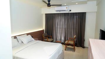 Una habitación de hotel con una cama, dos sillas, un escritorio, un equipo de aire acondicionado y un ventilador de techo.