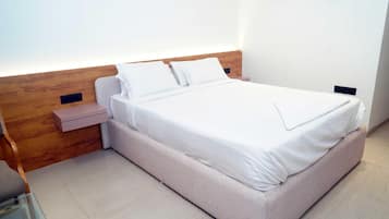 Una cama bien hecha con sábanas y almohadas blancas, un cabecero de madera y una mesita de noche con un cajón.