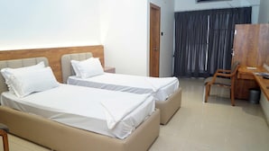 A hotel room with two beds, a desk, and a chair. - Deluxe Hotel Utkarsh (Silvassa)