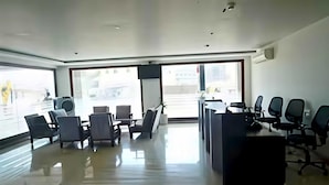 A modern office space with a reception desk, several chairs, and a large window providing a view of the outside. - Deluxe Hotel Utkarsh (Silvassa)