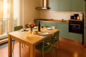 Comedor con mesa de madera dispuesta para cuatro, sillas verdes y un jarrón con flores.