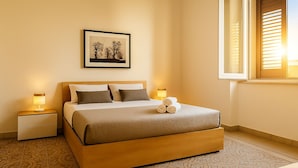 Una habitació d'hotel ben ordenada amb un llit, làmpades de nit, un quadre amb marc a la paret i una finestra amb persianes.