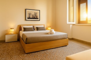 Habitación de hotel ordenada con cama, lámparas de noche, un cuadro en la pared y una ventana con persianas.