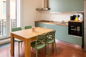 A modern kitchen with a wooden table and green chairs, a built-in oven, and a window with a view. - Le Residenze dell'Alloro - Gorizia Home (Palermo)