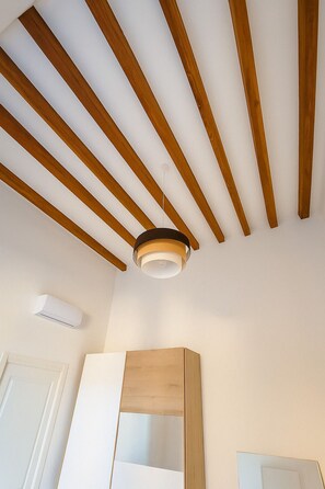A room with a sloped ceiling featuring wooden beams, a ceiling light fixture, and a white air conditioning unit. - Residenze dell'Alloro - Gorizia House (Palermo)