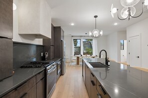 A modern kitchen with a central island, stainless steel appliances, and a chandelier. - Stunning Nash retreat w/ hot tub and rooftop view! (Nashville)