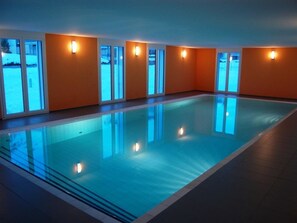 A large indoor swimming pool with clear glass walls and a tiled floor, surrounded by orange walls and windows. - Mühlehof D4 Appartement/Fewo, Dusche oder Bad, WC 4 1/2-Zimmerwohnung by Interhome (Davos)