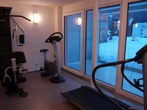 A home gym with exercise equipment, including a treadmill, stationary bike, and elliptical, with large windows providing a view of the outside. - Mühlehof D4 Appartement/Fewo, Dusche oder Bad, WC 4 1/2-Zimmerwohnung by Interhome (Davos)