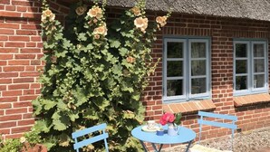 Un edificio de ladrillo con techo de paja, una ventana con molduras blancas y una maceta con flores.