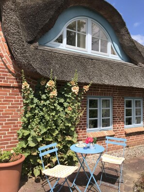 A brick building with a thatched roof, a window with white trim, and a potted plant with flowers. - Vrbo Property (Hasselberg OT Bobeck)