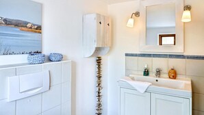 Un baño con un lavamanos blanco, un espejo y un cuadro enmarcado sobre el espejo.