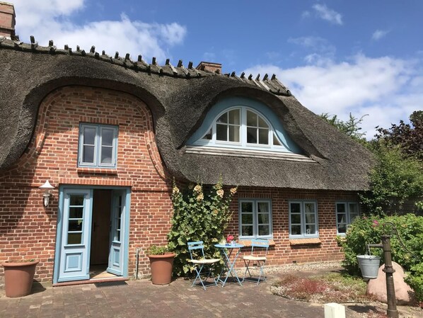 A brick house with a thatched roof, a blue door, and a small outdoor seating area with a table and chairs. - Vrbo Property (Hasselberg OT Bobeck)