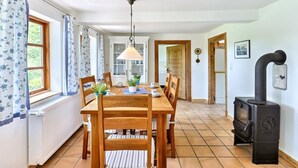 Comedor con mesa y sillas de madera, lámpara colgante y estufa de leña negra.