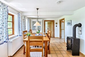 A dining area with a wooden table and chairs, a hanging light fixture, and a black wood-burning stove. - Vrbo Property (Hasselberg OT Bobeck)