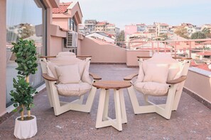 A balcony with two beige chairs and a small table, a potted plant, and a view of a cityscape. - Carlsen, Goat, Unique, Full City View Terrace (Istanbul)
