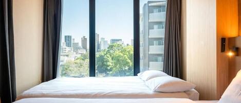 A hotel room with a large bed, a window with curtains, and a view of the cityscape.