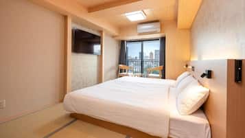Una habitación de hotel con una cama grande, una ventana con vistas a edificios, un ventilador de techo y un equipo de aire acondicionado de pared.