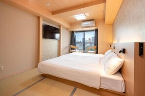 A hotel room with a large bed, a window with a view of buildings, a ceiling fan, and a wall-mounted air conditioning unit. - WELLSTAY Shinsekai Wakyo (Osaka)