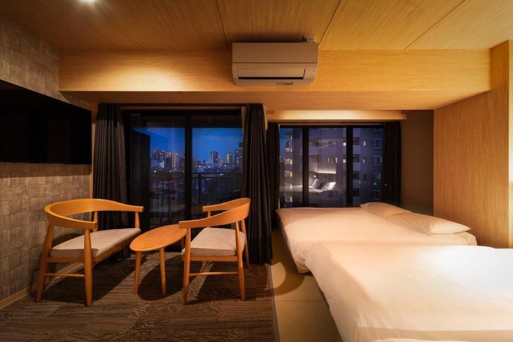 A hotel room with a bed, two chairs, a small table, and a view of the city at night.