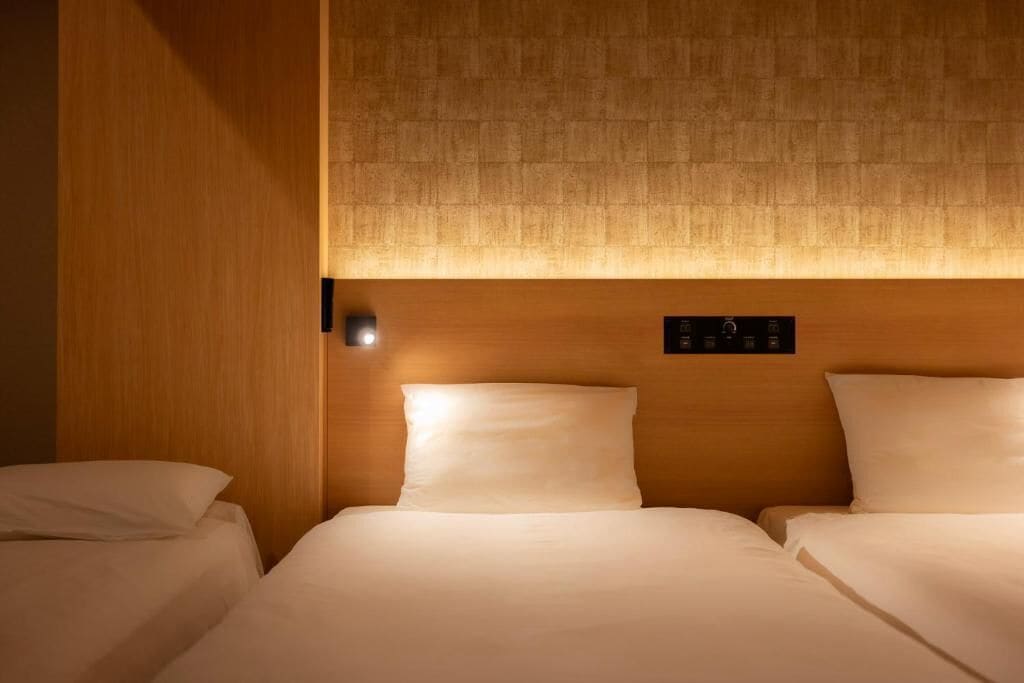 A hotel room with a wooden headboard, a control panel, and two beds with white bedding.