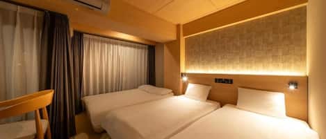 A hotel room with two beds, a desk, and an air conditioning unit.